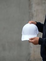 Person wearing black jacket holding white baseball cap against concrete wall background, suitable for branding, merchandise mockups, promotional campaigns, and apparel marketing.