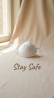 White N95 respirator mask on soft fabric near a window with Stay Safe text, promoting health protection and pandemic awareness.