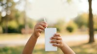 Young child with medium skin tone holding blank white card outdoors in park setting, suitable for advertising, marketing campaigns, educational materials, and promotional content.