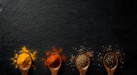 Colorful spices in wooden spoons arranged on dark slate background for culinary cooking and seasoning recipes.
