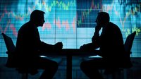 Silhouettes of two businessmen discussing at table against financial market chart background showing stock market volatility and trading analysis.