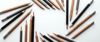 Assorted wooden and black pencils arranged around blank white paper on clean surface for creative drawing and sketching projects.