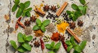 Aromatic spices and herbs arranged on rustic stone surface with mint leaves, cinnamon sticks, star anise, turmeric, coriander seeds for culinary cooking.