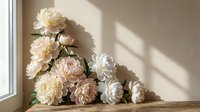 Soft white and blush pink peonies arranged on a wooden surface against a warm beige wall with gentle sunlight shadows.