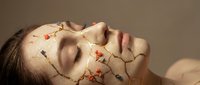 Young Caucasian woman with closed eyes, golden cracked lines and tiny dried flowers on her face, kintsugi-inspired art concept on neutral background.