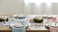 Elegant Easter table setting with pastel plates, decorative eggs, flowers and spring decor on wooden dining table for holiday celebration.