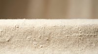 Natural beige linen fabric texture with loose threads and fibers, soft organic cotton material background for textile design and crafting projects.