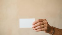 Male hand holding blank white business card against neutral beige background for corporate branding and marketing purposes.