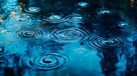 Raindrops creating concentric circles on dark blue water surface with reflections of evening sky, forming mesmerizing ripple patterns in tranquil puddle.