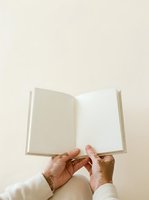 Open book with blank pages held by hands of an older adult wearing a cream-colored long-sleeved shirt against a neutral beige background. Suitable for education, publishing, and writing concepts.