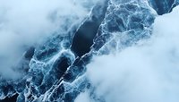 Dramatic aerial view of dark ocean waves with white foam creating abstract patterns against misty atmosphere in cold blue tones. Perfect for nature backgrounds.