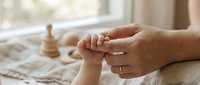 Tender moment of parent holding baby's tiny hand in soft natural light. Newborn care, bonding, family connection, parenting love, gentle touch, peaceful nursery setting.