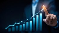 Business professional pointing at glowing growth chart showing increasing trend with blue bar graph and upward line graph on dark background for financial success concept.