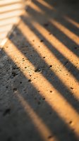 Warm golden sunlight casting dramatic parallel shadows across textured sand surface with natural grain details creating abstract geometric pattern for backgrounds.