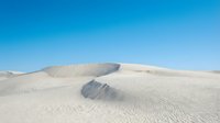 Vast white sand dunes with rippled textures under clear blue sky, showcasing desert landscape and natural patterns for travel and nature backgrounds.