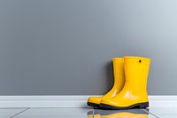 Yellow rain boots against gray wall on white floor, minimalist composition with reflection creates modern, clean aesthetic for lifestyle and weather concepts.