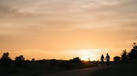 Silhouettes of family standing together on rural road at golden sunset with warm sky and trees, representing togetherness and outdoor lifestyle.
