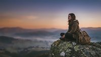 Woman hiker sitting on mountain rock at sunrise, overlooking misty valley landscape. Adventure travel and outdoor exploration concept for nature enthusiasts.