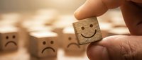 Hand selecting wooden cube with happy smiley face from group of sad face blocks representing positive choice, optimism and emotional wellbeing concept.