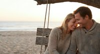 Young Caucasian couple in love sharing intimate moment on beach swing at sunset, romantic vacation getaway lifestyle.