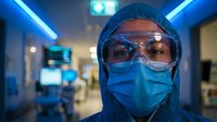 Healthcare worker in protective equipment with safety goggles and face mask in modern medical facility with blue lighting atmosphere.
