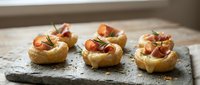 Gourmet appetizers with prosciutto and figs on pastry shells served on slate board for elegant entertaining and fine dining occasions.