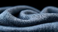 Soft waves of dark gray fabric create gentle folds and curves against black background, showcasing textile texture and minimalist composition for fashion and design projects.