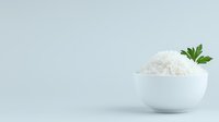 Minimalist composition of steamed white rice served in ceramic bowl garnished with fresh parsley leaf against light background, copy space for text.