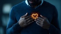 African American man in navy sweater with glowing heart light emanating from chest against dark background, representing love, emotion, and inner light.
