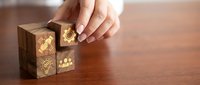 Hand placing wooden cube with golden business icons on desk representing strategic planning and corporate growth solutions.