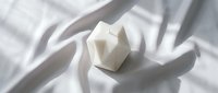 Geometric white stone or marble cube on draped white fabric with soft shadows, suitable for minimalist design, luxury branding, and contemporary product backgrounds.