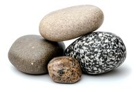 Smooth river stones and speckled granite pebbles arranged in balanced composition on white background, showing natural texture and mineral patterns.