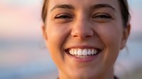 Happy young Caucasian woman with bright smile and perfect white teeth enjoying golden hour sunlight outdoors with natural glowing skin and joyful expression.