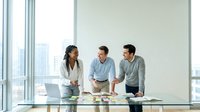 Professional diverse business team collaborating at modern glass conference table in bright office with city skyline view during strategic planning meeting.