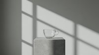 Clear glass cup with handle on cylindrical concrete pedestal, minimalist composition with window light casting geometric shadows on neutral wall, suitable for beverage, lifestyle and interior design projects.