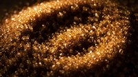 Macro shot of golden glitter particles with shallow depth of field, creating an abstract sparkly texture with warm metallic tones and bokeh effects.