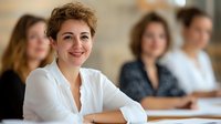 Confident young businesswoman with curly hair smiling at camera during corporate meeting with female colleagues in modern office environment.
