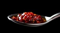 Red chili flakes and crushed peppers on silver spoon against dark background, dramatic lighting highlights spicy seasoning texture and vibrant color.