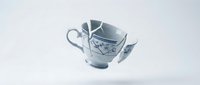 Broken ceramic teacup with handle and saucer shattered into pieces on white background, symbolizing fragility, loss, or damage for design and editorial projects.