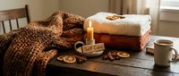 Cozy self care flat lay with candle, folded towels, dried oranges, cinnamon, knit blanket and coffee on rustic wooden table.