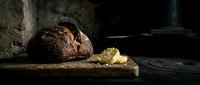 Freshly baked dark rye bread loaf with crumbs on wooden surface in rustic kitchen setting, suitable for bakery, food, and culinary content.