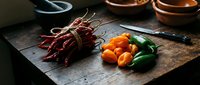 Fresh red chili peppers and colorful vegetables on rustic wooden cutting board in moody kitchen lighting for culinary cooking and food preparation.