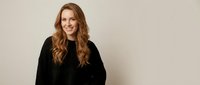 Smiling redhead woman in black sweater sitting casually against neutral background for lifestyle and portrait photography projects.