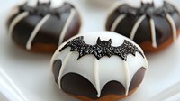 Halloween donuts decorated with black and white icing featuring bat silhouettes and sparkly details on white plate, festive holiday treats for party dessert table.