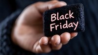 Hand holding small black chalkboard with pink Black Friday text written on it against dark background, promotional seasonal shopping concept.