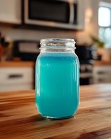 Vibrant turquoise blue cocktail or summer drink in mason jar on wooden kitchen counter, refreshing beverage with clean modern aesthetic and soft bokeh background.