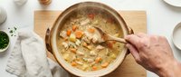 Homemade chicken soup with vegetables and noodles in ceramic bowl, hand holding wooden spoon, comfort food for cold weather and wellness.