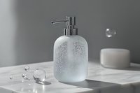 Modern frosted glass soap dispenser with chrome pump on marble surface in minimalist bathroom setting with water droplets and clean aesthetic.
