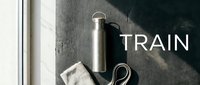 Stainless steel water bottle with towel and jump rope on concrete surface, fitness and hydration concept for training.
