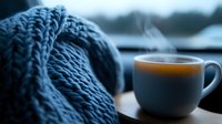 Steaming coffee cup next to cozy knitted scarf by window on rainy day, creating atmospheric mood with soft natural lighting and bokeh effect.